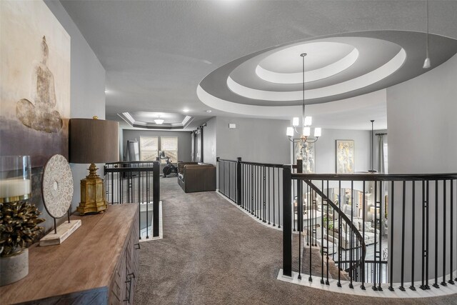 corridor featuring an inviting chandelier, carpet flooring, and a tray ceiling