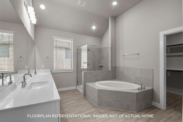 full bathroom featuring a stall shower, a walk in closet, a sink, and wood finished floors