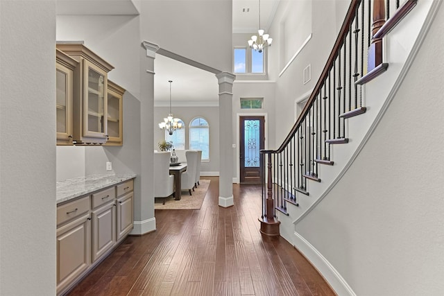 entrance foyer with decorative columns, dark hardwood / wood-style floors, a chandelier, and a towering ceiling