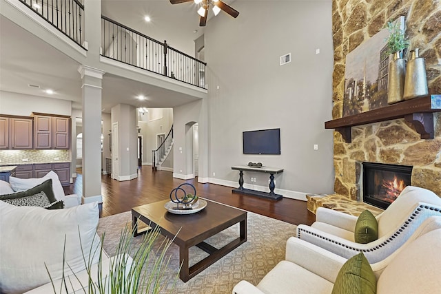 living room featuring a fireplace, dark hardwood / wood-style floors, ceiling fan, and ornate columns