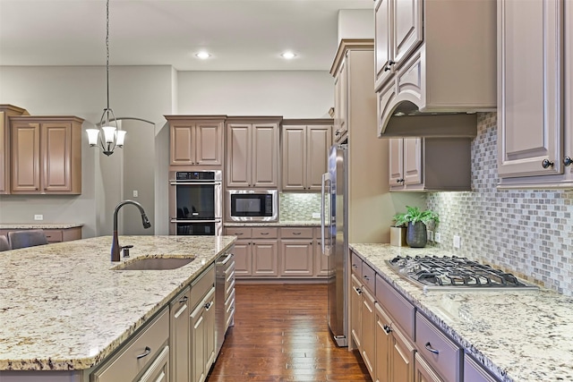 kitchen featuring pendant lighting, sink, appliances with stainless steel finishes, a kitchen island with sink, and light stone counters