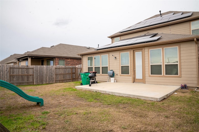 back of property with a playground, solar panels, a yard, and a patio area