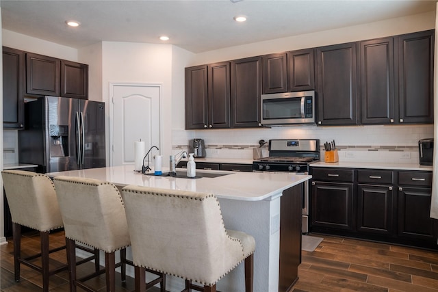 kitchen featuring appliances with stainless steel finishes, a center island with sink, a kitchen breakfast bar, and decorative backsplash