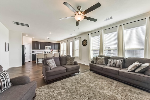 living room with ceiling fan, dark wood-style flooring, visible vents, and baseboards