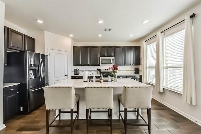 kitchen featuring visible vents, a kitchen breakfast bar, light countertops, appliances with stainless steel finishes, and a center island with sink