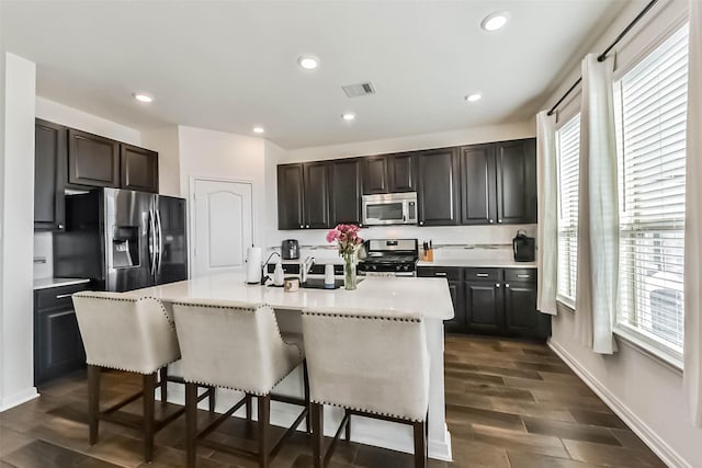 kitchen featuring a breakfast bar, wood finish floors, light countertops, visible vents, and appliances with stainless steel finishes