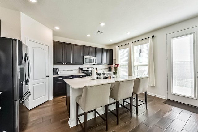 kitchen with visible vents, dark wood finished floors, stainless steel appliances, light countertops, and a kitchen bar