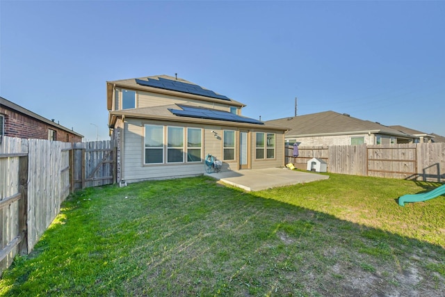 back of house with a patio area, a fenced backyard, roof mounted solar panels, and a lawn