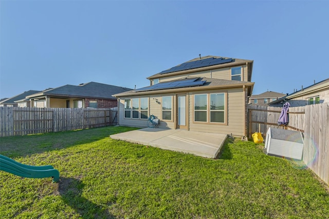 rear view of house with a patio area, a fenced backyard, roof mounted solar panels, and a lawn