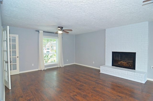 unfurnished living room with ceiling fan, a textured ceiling, baseboards, a brick fireplace, and dark wood finished floors