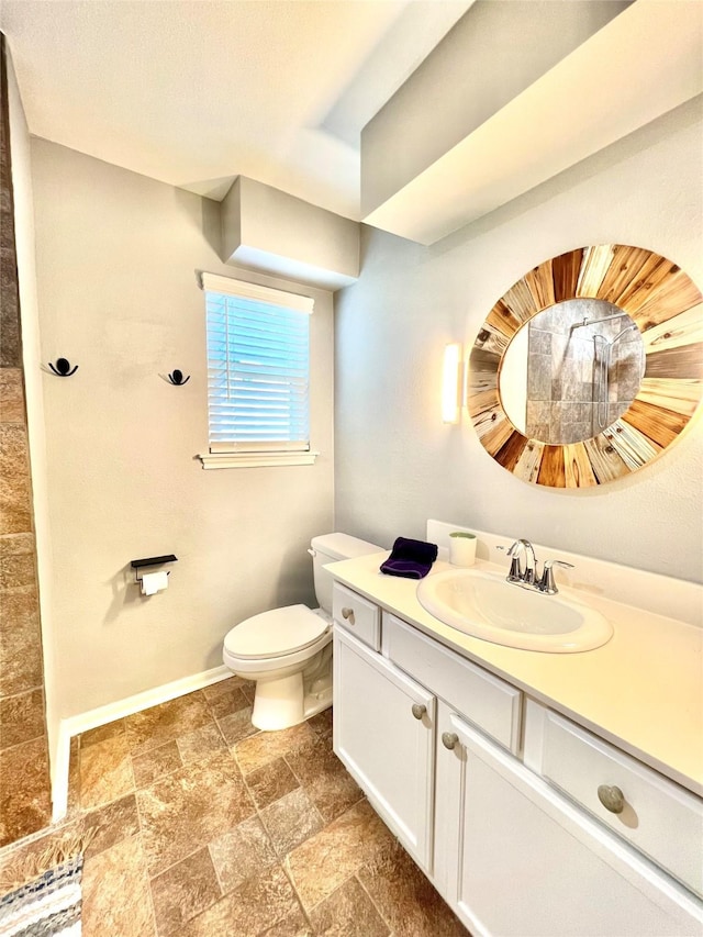 bathroom with toilet, stone finish flooring, baseboards, and vanity