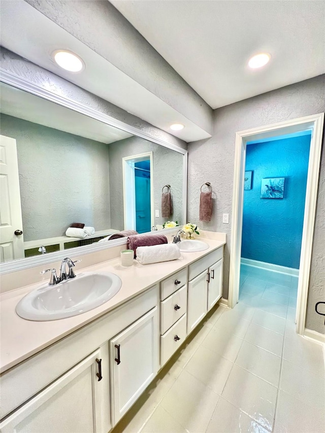 full bath with a textured wall, tile patterned floors, a sink, and double vanity