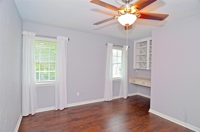 unfurnished room with dark wood-style flooring, plenty of natural light, built in desk, and baseboards