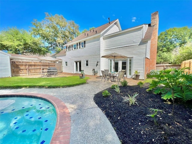 rear view of house with a fenced in pool, a patio, a fenced backyard, a chimney, and a yard