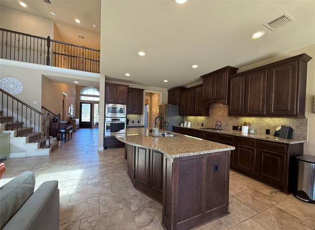 kitchen featuring an island with sink, appliances with stainless steel finishes, dark brown cabinets, and decorative backsplash