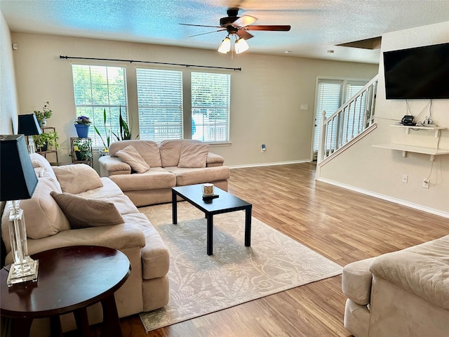 living room featuring ceiling fan, a textured ceiling, and light wood-type flooring