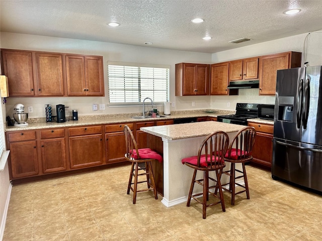 kitchen featuring sink, a breakfast bar area, a kitchen island, light stone countertops, and black appliances