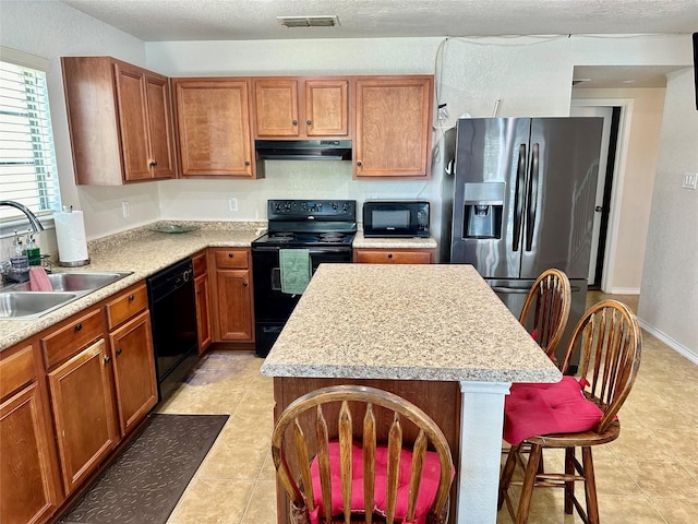 kitchen featuring sink, black appliances, a center island, and a breakfast bar