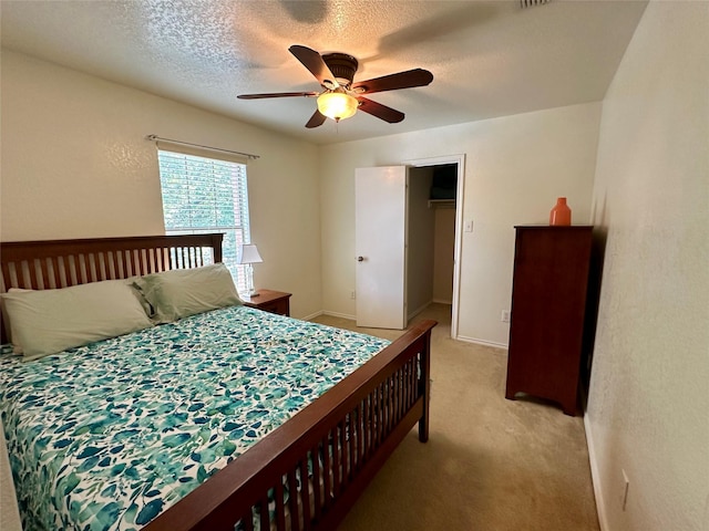 carpeted bedroom with ceiling fan, a walk in closet, a textured ceiling, and a closet