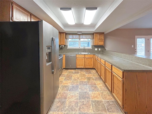 kitchen featuring appliances with stainless steel finishes, dark countertops, a raised ceiling, and brown cabinets