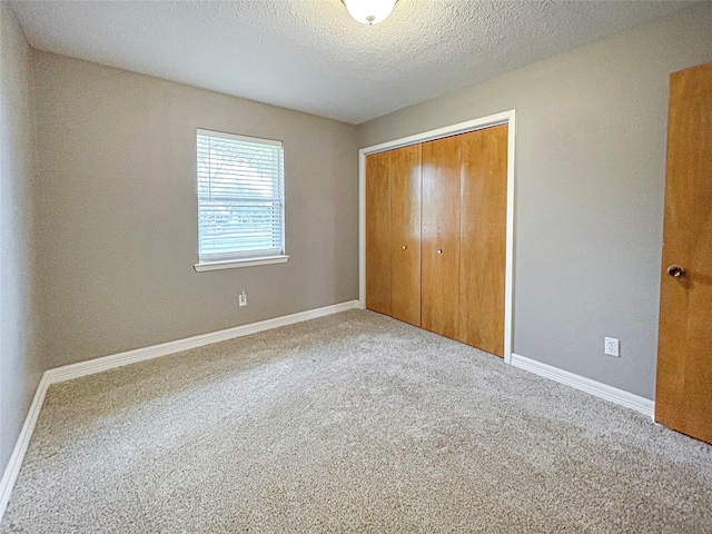 unfurnished bedroom with a textured ceiling, a closet, carpet flooring, and baseboards