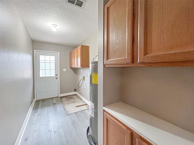 laundry room with cabinet space, visible vents, a textured ceiling, light wood-type flooring, and water heater