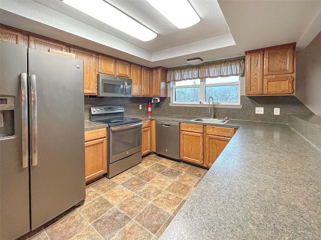 kitchen with appliances with stainless steel finishes, a tray ceiling, a sink, and tasteful backsplash