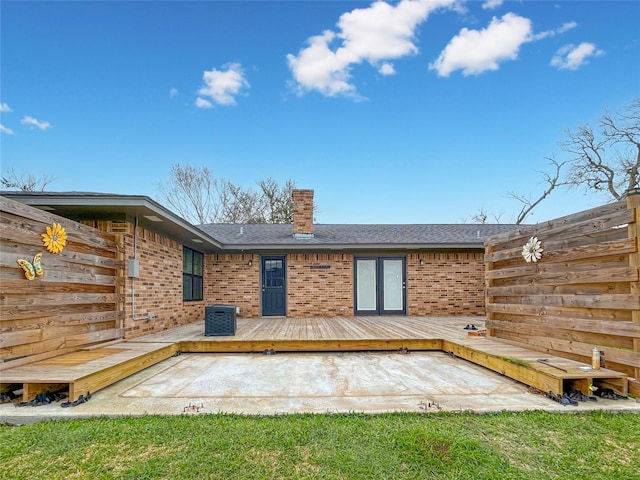 rear view of property with a deck, brick siding, fence, roof with shingles, and a chimney