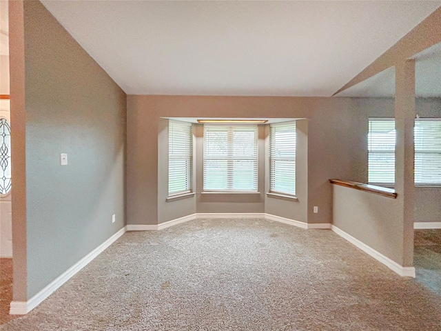 carpeted empty room with vaulted ceiling and baseboards