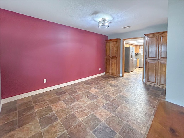 empty room featuring a textured ceiling, stone finish flooring, visible vents, and baseboards