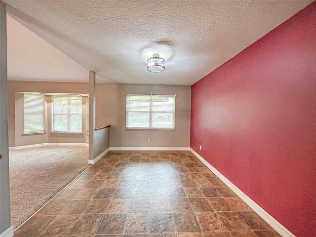 spare room featuring a textured ceiling, stone finish floor, and baseboards