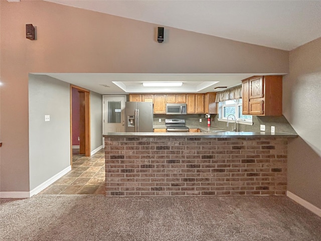 kitchen featuring brown cabinets, stainless steel appliances, light colored carpet, light countertops, and a peninsula