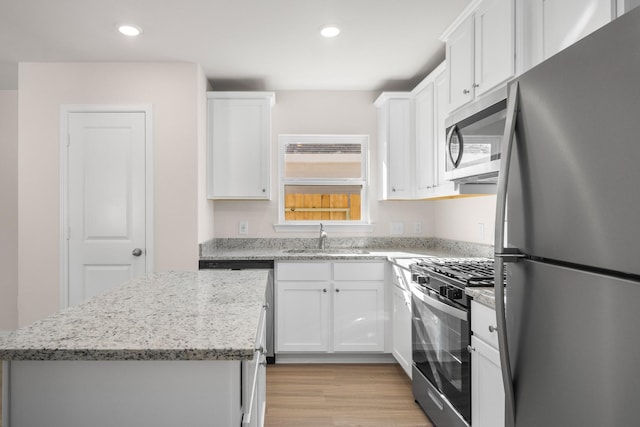 kitchen with sink, white cabinetry, appliances with stainless steel finishes, a kitchen island, and light stone countertops