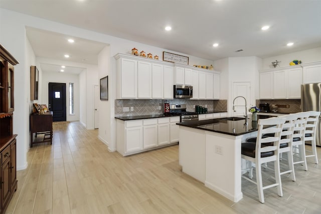 kitchen with stainless steel appliances, a kitchen island with sink, sink, and white cabinets