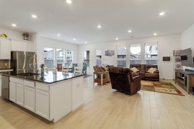 kitchen with an island with sink, sink, white cabinets, stainless steel appliances, and light hardwood / wood-style flooring