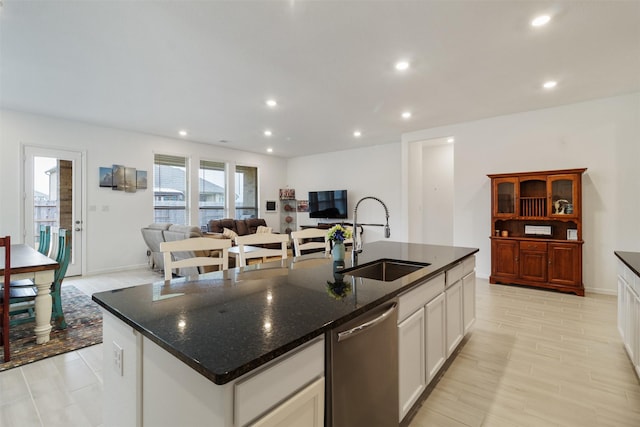 kitchen featuring sink, a center island with sink, dishwasher, dark stone counters, and white cabinets