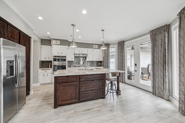 kitchen featuring an island with sink, appliances with stainless steel finishes, white cabinets, and decorative light fixtures