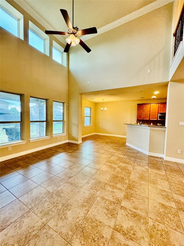 unfurnished living room with ceiling fan with notable chandelier, ornamental molding, and light tile patterned flooring