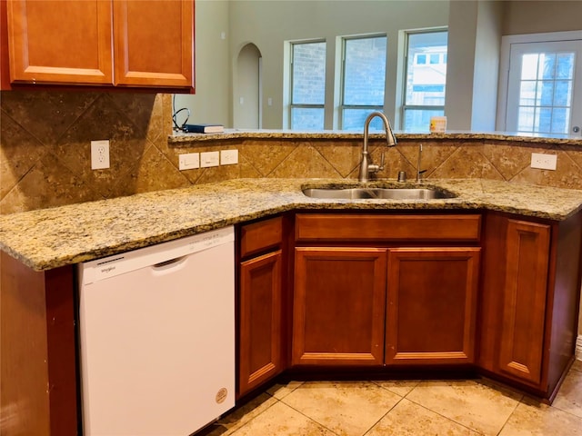 kitchen featuring dishwasher, sink, light stone countertops, and backsplash