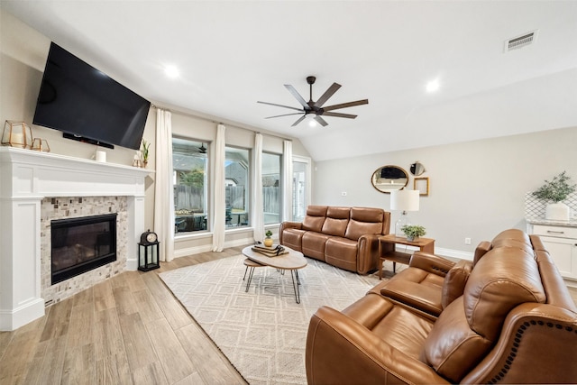 living room featuring a tiled fireplace, vaulted ceiling, ceiling fan, and light wood-type flooring