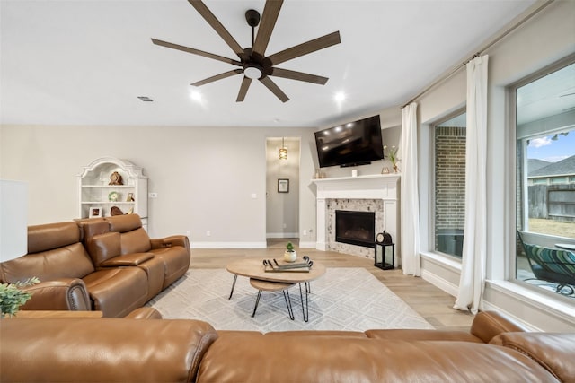 living room with ceiling fan, a stone fireplace, and light hardwood / wood-style flooring