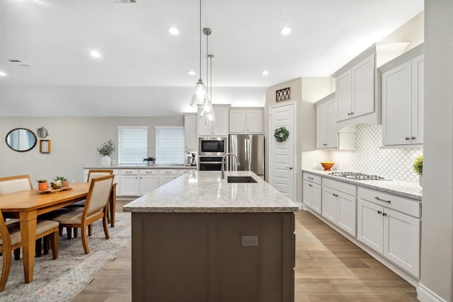 kitchen with decorative light fixtures, tasteful backsplash, an island with sink, white cabinets, and stainless steel appliances