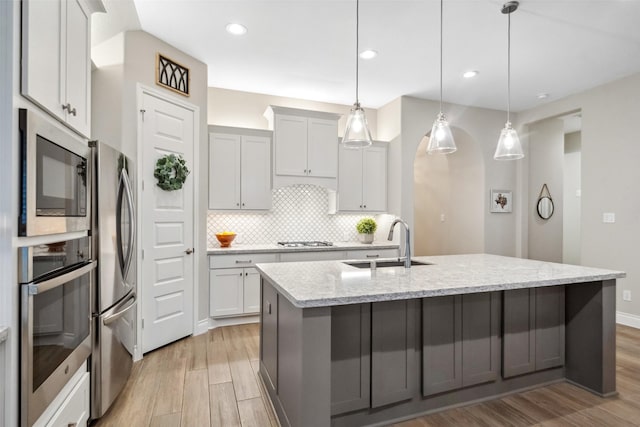 kitchen with sink, light stone counters, decorative light fixtures, appliances with stainless steel finishes, and a kitchen island with sink