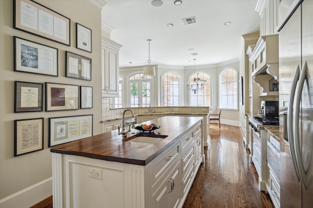 kitchen featuring sink, butcher block counters, an island with sink, white cabinets, and decorative light fixtures