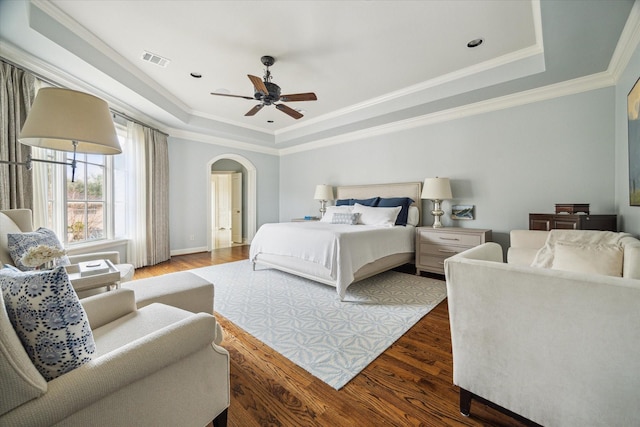 bedroom featuring a raised ceiling, ornamental molding, and dark wood-type flooring