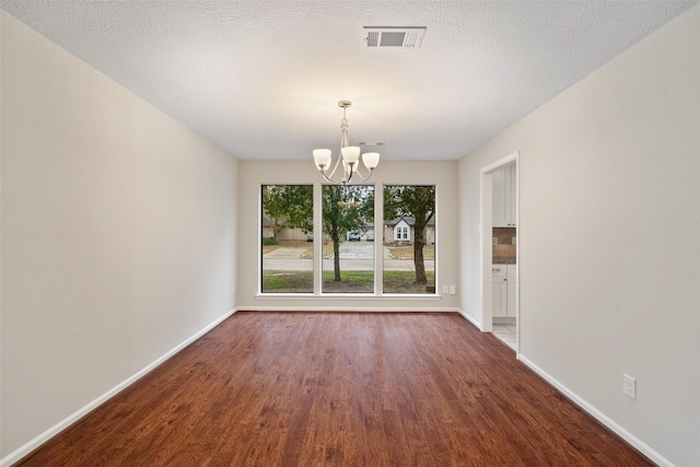 unfurnished dining area with dark hardwood / wood-style flooring, a textured ceiling, and a chandelier