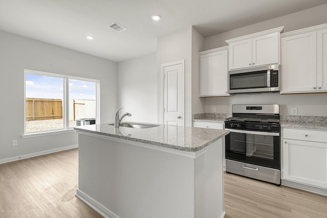 kitchen with sink, white cabinetry, a center island with sink, stainless steel appliances, and light stone countertops