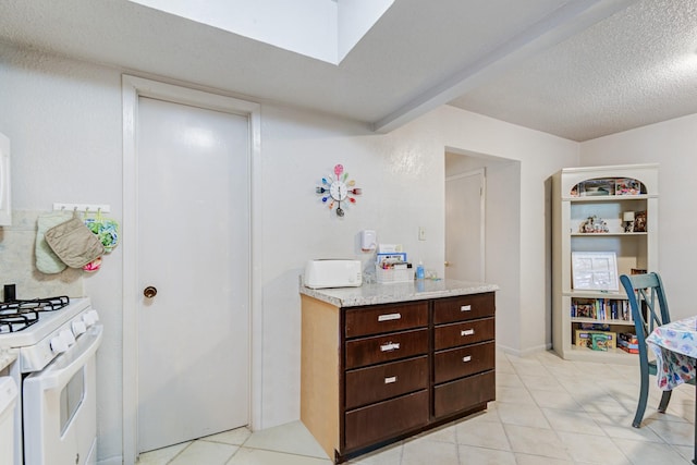 kitchen featuring light tile patterned floors, white gas stove, dark brown cabinets, and a textured ceiling