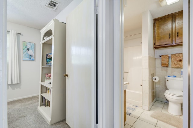 bathroom featuring a bath, a textured ceiling, tile patterned floors, and toilet