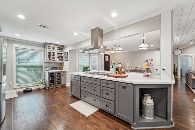 kitchen with stainless steel gas cooktop, gray cabinetry, crown molding, island range hood, and pendant lighting